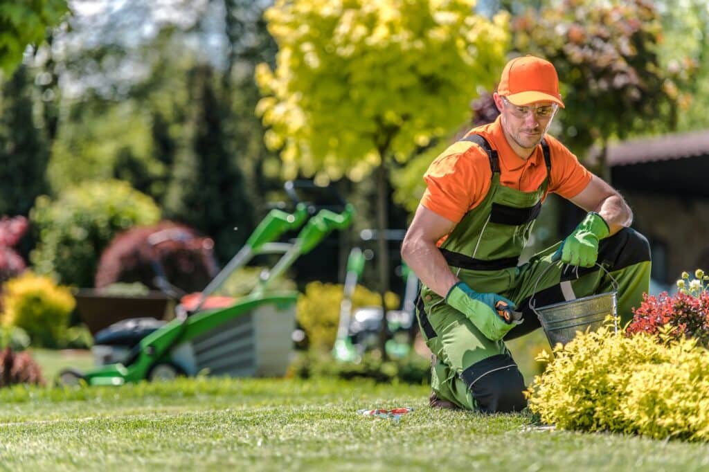 Jardinier en tenue orange et verte plantant des arbustes dans un jardin coloré.