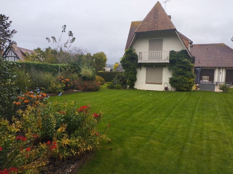 Vue d'un jardin luxuriant avec fleurs colorées devant une maison blanche, montrant une pelouse parfaitement entretenue.